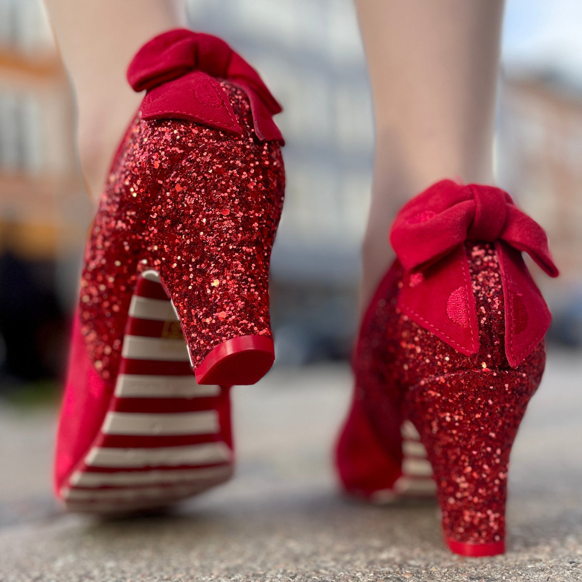 Red glittery high-heeled shoes with bows on a blurred background