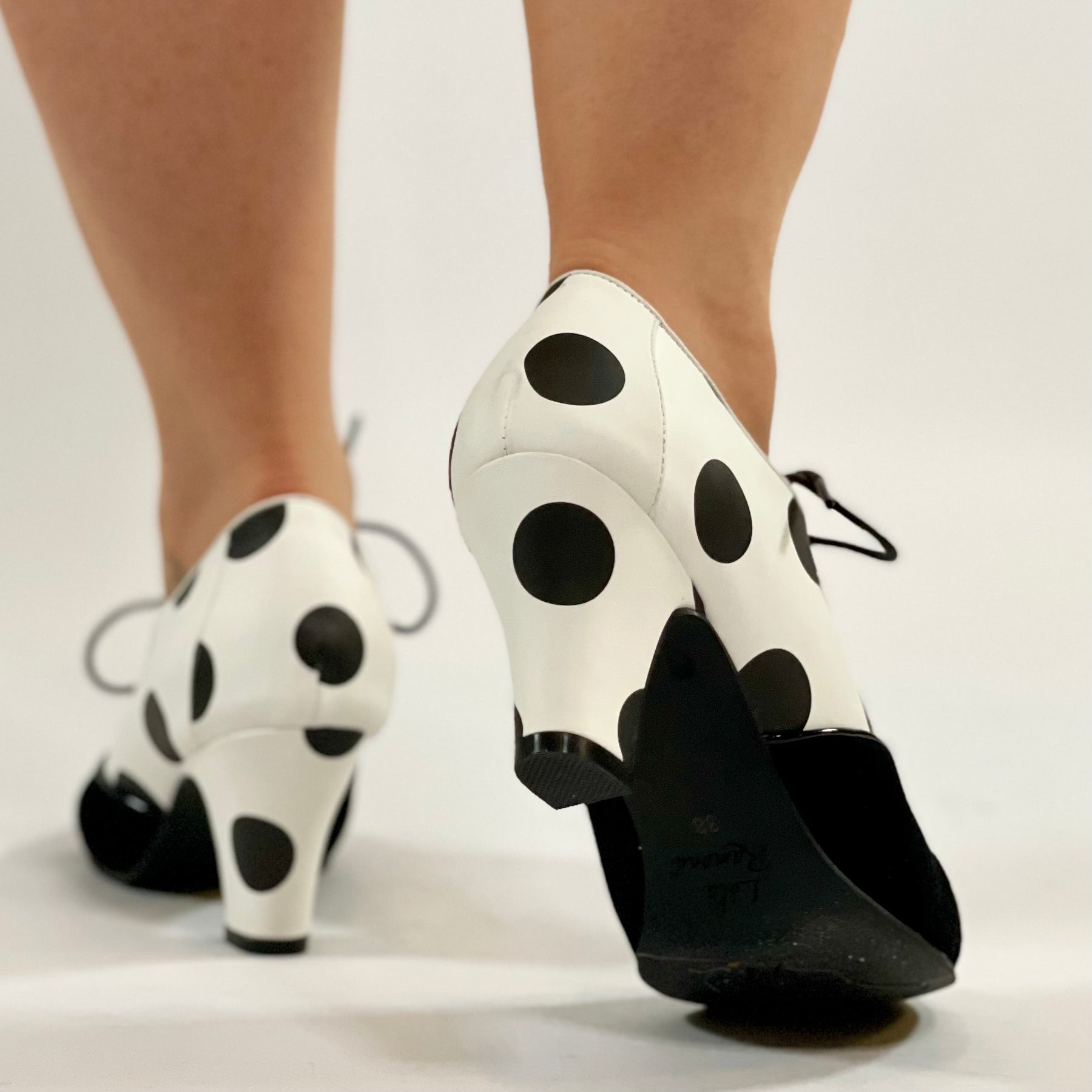 A pair of women's shoes with black and white polka dot pattern on the upper, featuring a suede covered toe and a rubber outsole.