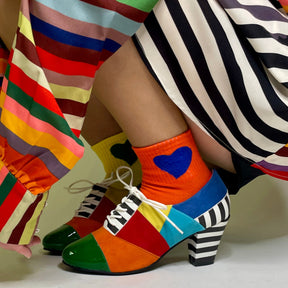 Colorful patchwork shoes with a heart design on socks, worn by people in striped pants.