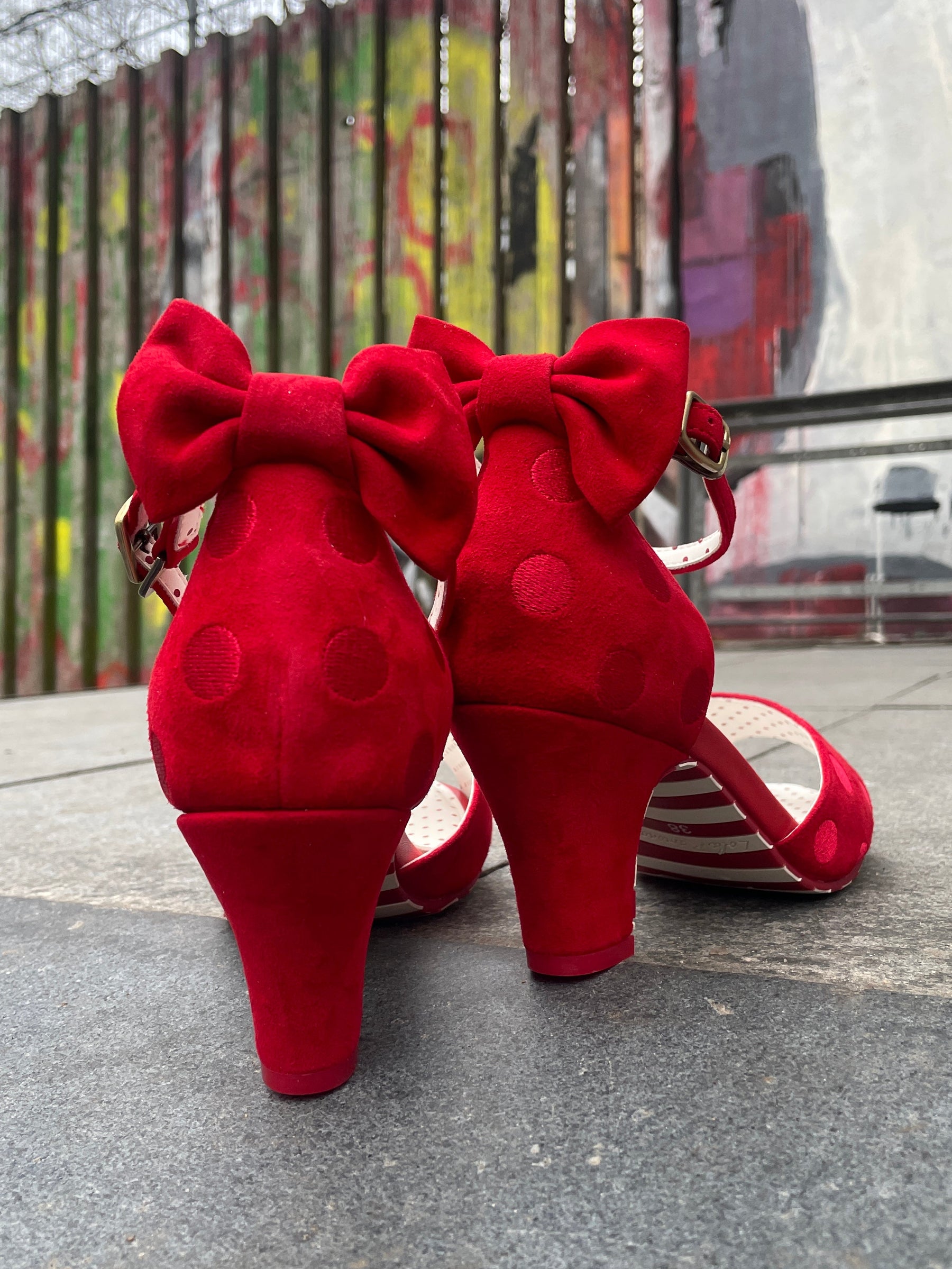 Red shoes with white soles on a concrete surface next to a colorful mural.