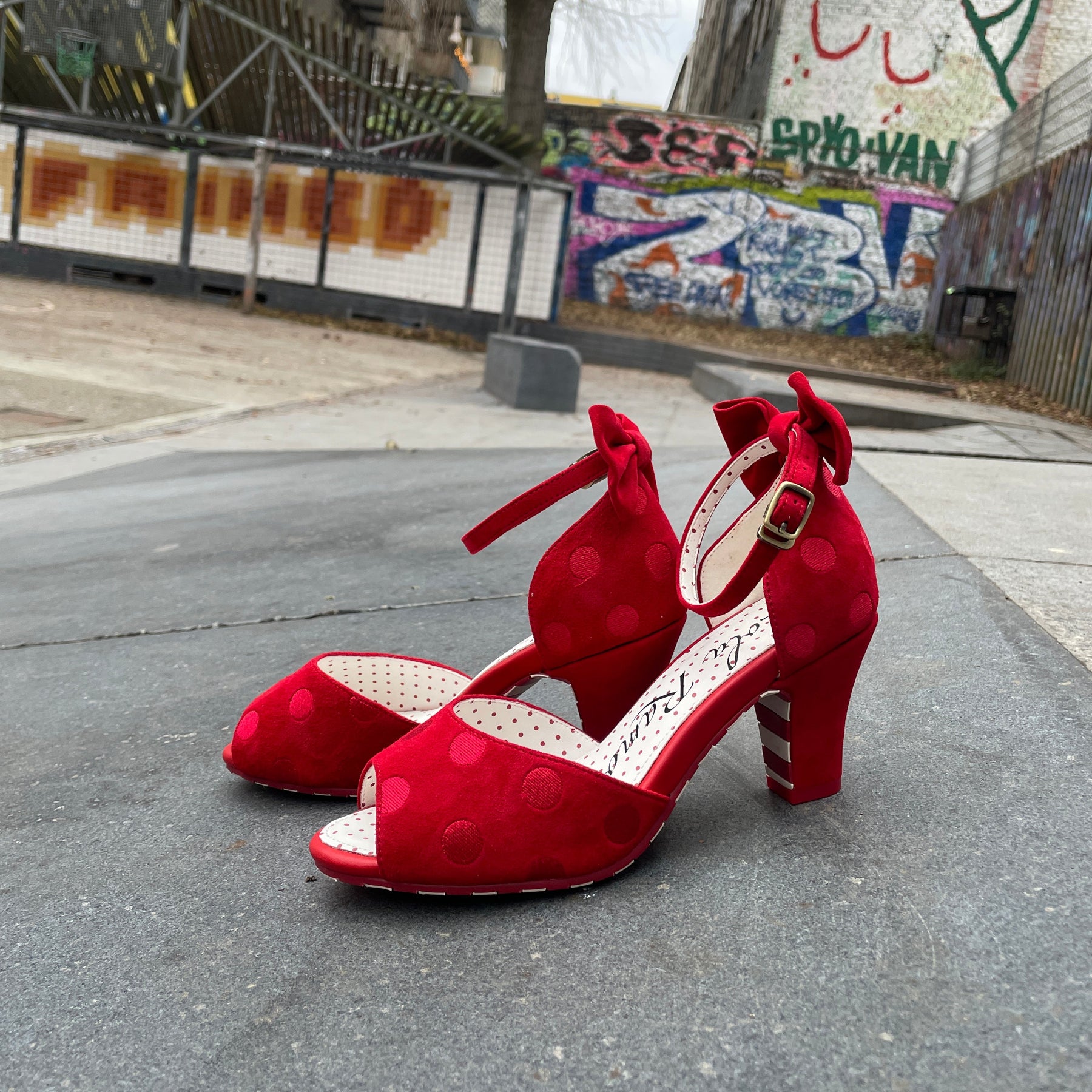 Red high-heeled shoe with white sole on a concrete surface near a wall with graffiti.